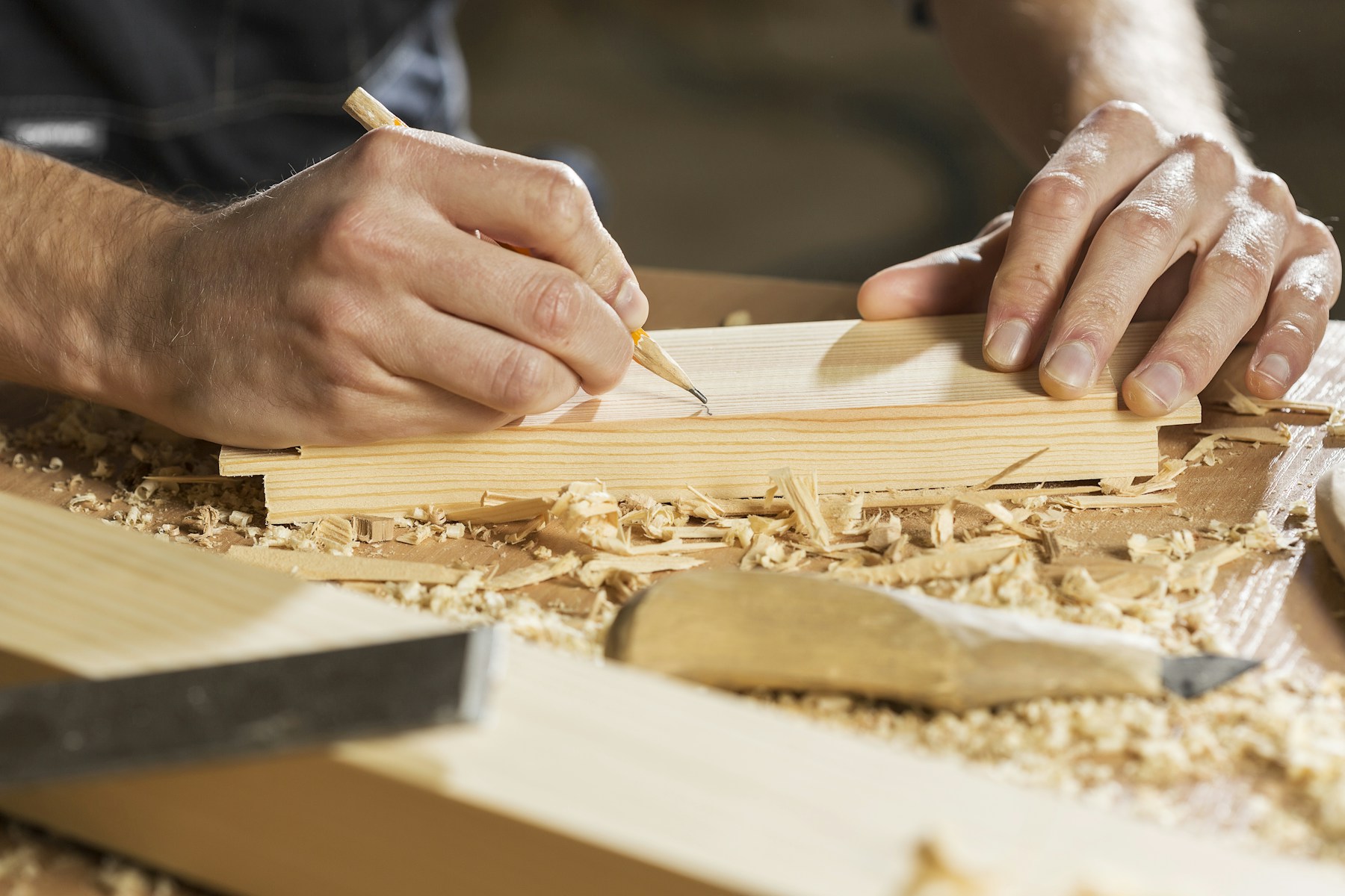 Close-up of hands marking a timber board, illustrating careful carpentry